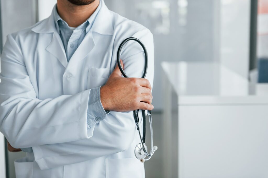 Stethoscope in hands. Professional medic in white coat is in the clinic