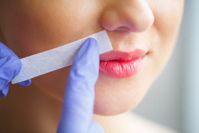 Close-up of eyebrow waxing with a wax strip, showing the discomfort of traditional hair removal methods
