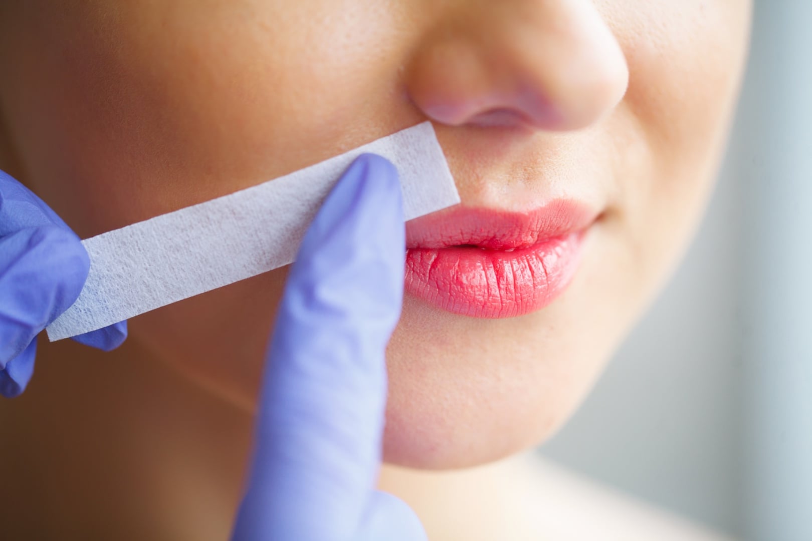 Close-up of eyebrow waxing with a wax strip, showing the discomfort of traditional hair removal methods